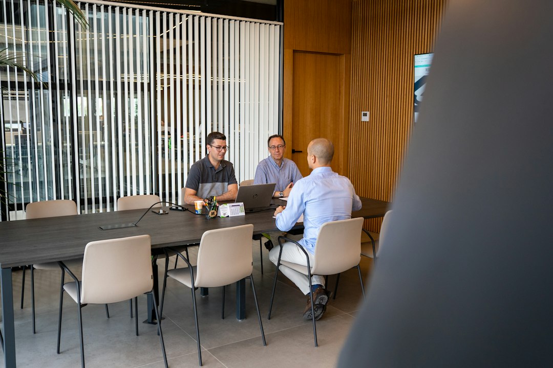 Deux professionnels reçoivent un client autour d’une table de réunion, dans leurs bureaux.