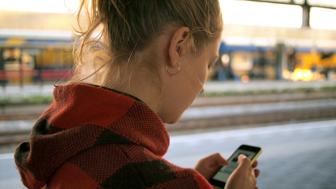 Une jeune femme consulte son smartphone sur un quai de gare.