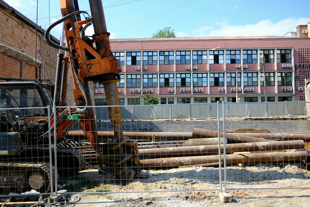 Une foreuse sur un chantier de fondations, derrière une clôture de chantier.