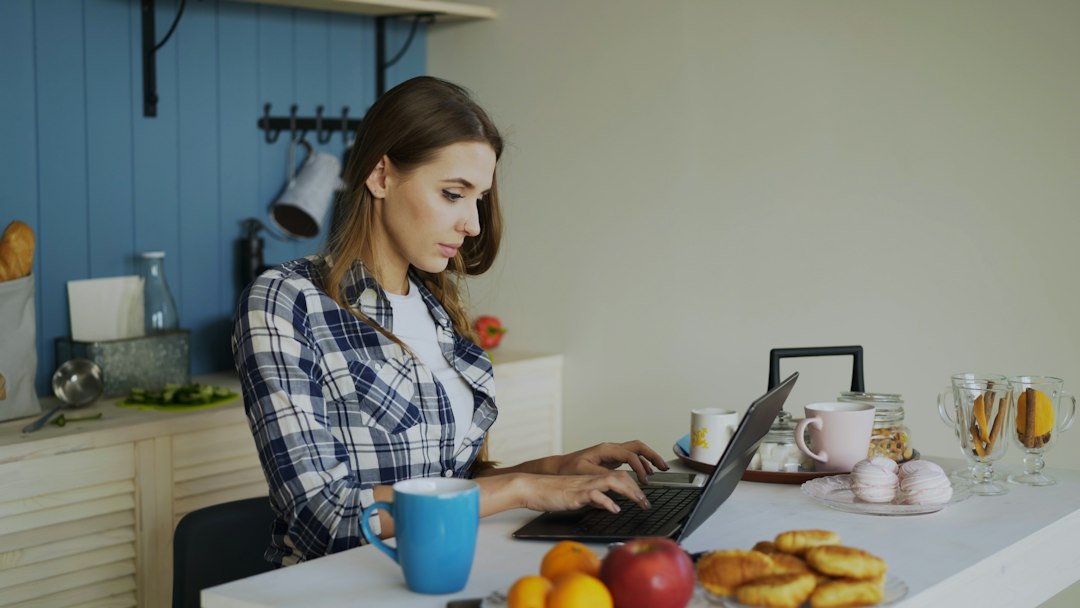 Une jeune femme tape sur son ordinateur portable à la table de sa cuisine.